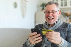mayor hombre compras en línea participación teléfono inteligente pago con crédito tarjeta. antiguo abuelo comprando en Internet entrar crédito tarjeta detalles. en línea compras entrega Servicio más viejo Generacion moderno tecnología uso foto