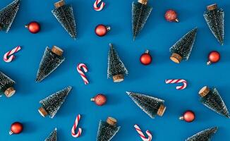 Trendy Christmas pattern made with green Christmas trees, candy canes and red Xmas baubles on blue background. Minimal creative Christmas and New Year concept. Festive holiday backdrop. Flat lay. photo
