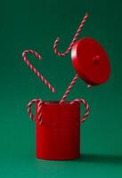Christmas candy canes coming out of red Xmas tin decorated with classic bells against green background. Minimal Christmas and New Year concept. Creative festive holiday layout. Christmas aesthetic. photo