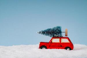 Winter composition made with red car with Christmas tree and snow on blue background. Minimal Christmas and New Year concept. Creative festive holiday layout. Xmas aesthetic. photo