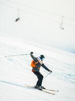 Close up dynamic sports banner of man skier on piste ski downhill fast motion in Alps. Active winter holidays, skiing downhill in overcast day. Ski rides on the track with swirls of fresh snow photo