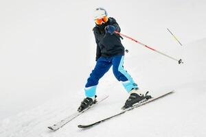 Young man learning to ski on a snowy slope having fun point finger to at camera while slowing down on snowy slope isolated photo
