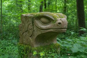 Moss covered stone sculpture of a reptilian creature in a lush forest photo