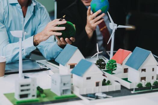 Engineers meeting about wind turbine model and house model. Renewable energy and housing development concept. Team of architects and engineers in modern office discussing design structure. photo
