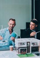 Engineers meeting about wind turbine model and house model. Renewable energy and housing development concept. Team of architects and engineers in modern office discussing design structure. photo