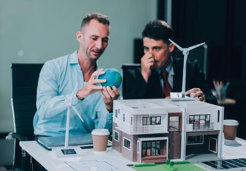 Engineers meeting about wind turbine model and house model. Renewable energy and housing development concept. Team of architects and engineers in modern office discussing design structure. photo