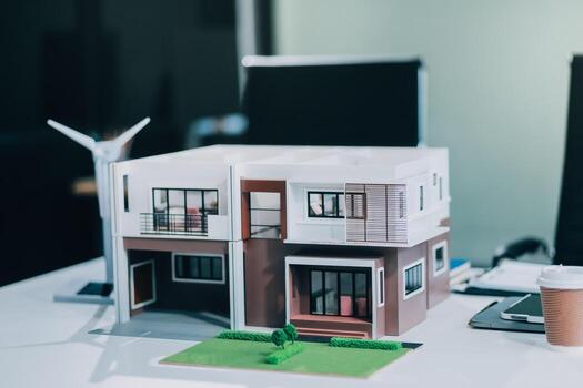 Engineers meeting about wind turbine model and house model. Renewable energy and housing development concept. Team of architects and engineers in modern office discussing design structure. photo