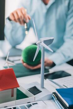 Engineers meeting about wind turbine model and house model. Renewable energy and housing development concept. Team of architects and engineers in modern office discussing design structure. photo