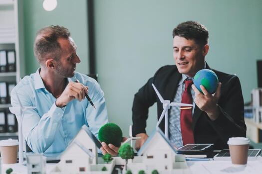 Engineers meeting about wind turbine model and house model. Renewable energy and housing development concept. Team of architects and engineers in modern office discussing design structure. photo