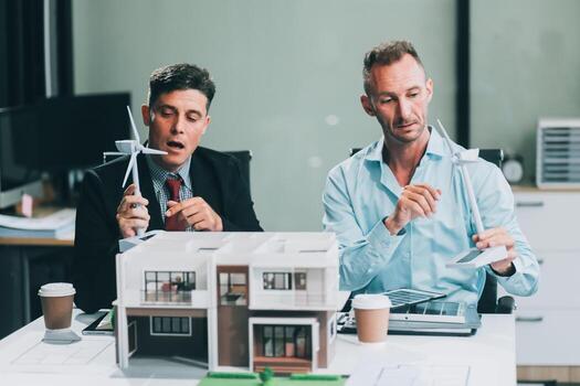 Engineers meeting about wind turbine model and house model. Renewable energy and housing development concept. Team of architects and engineers in modern office discussing design structure. photo