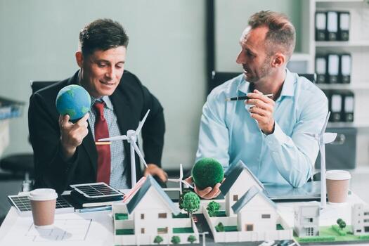 Engineers meeting about wind turbine model and house model. Renewable energy and housing development concept. Team of architects and engineers in modern office discussing design structure. photo