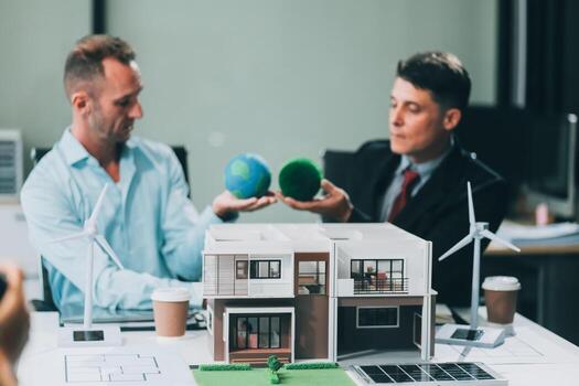 Engineers meeting about wind turbine model and house model. Renewable energy and housing development concept. Team of architects and engineers in modern office discussing design structure. photo