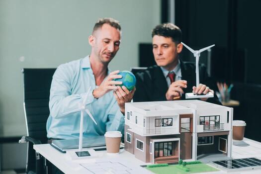 Engineers meeting about wind turbine model and house model. Renewable energy and housing development concept. Team of architects and engineers in modern office discussing design structure. photo