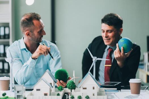 Engineers meeting about wind turbine model and house model. Renewable energy and housing development concept. Team of architects and engineers in modern office discussing design structure. photo