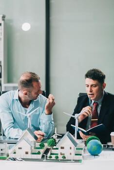 Engineers meeting about wind turbine model and house model. Renewable energy and housing development concept. Team of architects and engineers in modern office discussing design structure. photo