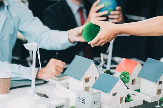 Engineers meeting about wind turbine model and house model. Renewable energy and housing development concept. Team of architects and engineers in modern office discussing design structure. photo