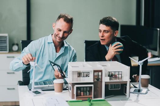 Engineers meeting about wind turbine model and house model. Renewable energy and housing development concept. Team of architects and engineers in modern office discussing design structure. photo