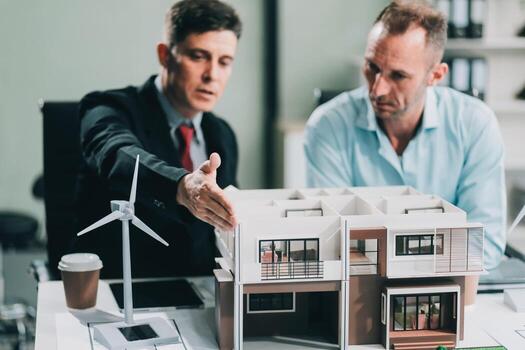 Engineers meeting about wind turbine model and house model. Renewable energy and housing development concept. Team of architects and engineers in modern office discussing design structure. photo