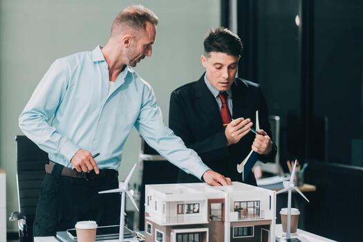 Engineers meeting about wind turbine model and house model. Renewable energy and housing development concept. Team of architects and engineers in modern office discussing design structure. photo