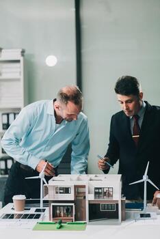 Engineers meeting about wind turbine model and house model. Renewable energy and housing development concept. Team of architects and engineers in modern office discussing design structure. photo