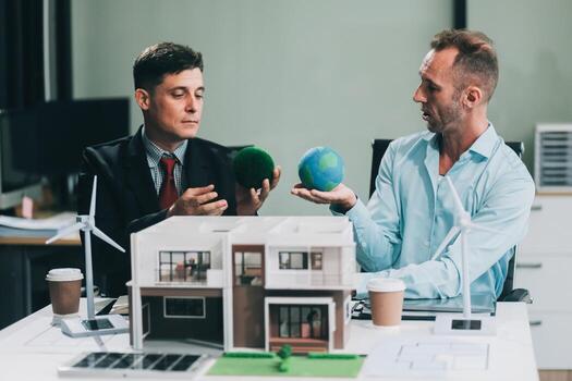 Engineers meeting about wind turbine model and house model. Renewable energy and housing development concept. Team of architects and engineers in modern office discussing design structure. photo