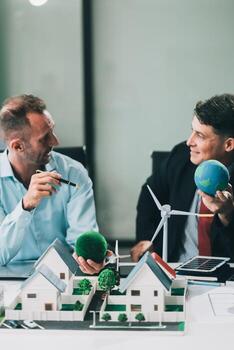 Engineers meeting about wind turbine model and house model. Renewable energy and housing development concept. Team of architects and engineers in modern office discussing design structure. photo