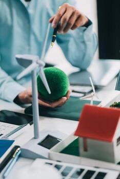 Engineers meeting about wind turbine model and house model. Renewable energy and housing development concept. Team of architects and engineers in modern office discussing design structure. photo