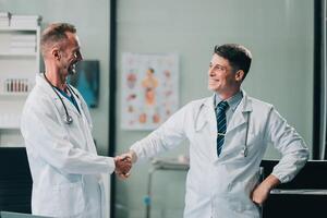 Smiling young male clinician shake hands with happy teammate appreciate for assistance on surgery show support respect on team council. Two doctors partners handshaking making deal reaching agreement photo