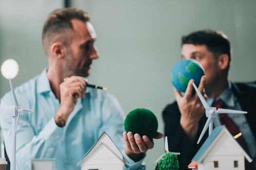 Engineers meeting about wind turbine model and house model. Renewable energy and housing development concept. Team of architects and engineers in modern office discussing design structure. photo