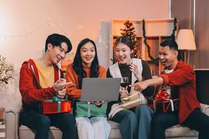 Group of young Asian man and women as friends having fun at a New Year's celebration, holding gift boxes standing by Christmas tree decoration, midnight countdown Party at home with holiday season. photo