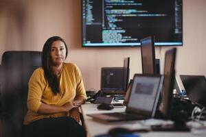 A businesswoman sitting in a programmer's office surrounded by computers, showing her expertise and dedication to technology. photo