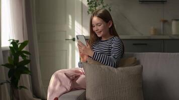 Little Caucasian girl holding mobile phone smartphone social media smiling laughing funny technology browser online child daughter networking connected scrolling virtual gadget device kid home sofa video