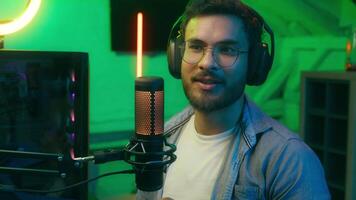 Smiling Indian man Hispanic male Arabian guy radio host presenter worker streamer gamer influencer talking in microphone talk in mic broadcasting influence working stream neon night room home computer video