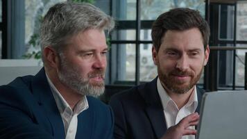 Close-up two joyful Caucasian men businessmen looking at computer screen discussing financial trading project at office meeting discuss presentation business partners conclude profitable deal contract video