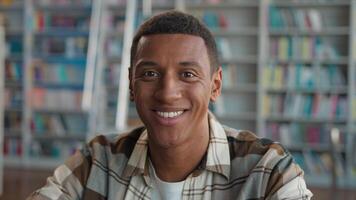 African American man student looking at camera toothy dental smile male ethnic library university study educational guy learning scholar college bookshelf academic bookworm reader intelligence smart video