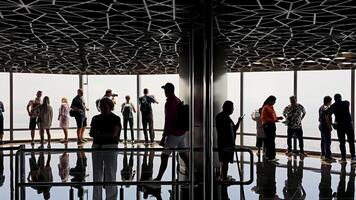 Dubai OAE 20.10.2024 Silhouettes of Tourists on Burj Khalifa Observation Deck, with a patterned ceiling overhead and reflections creating a dramatic and immersive scene against the bright daylight. video