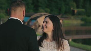 Bride Smiling at Groom in Green Park Setting, with warm sunlight casting a gentle glow over their romantic moment. video