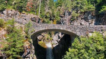 Mount Rainier National Park Stone bridge over a waterfall in a forest. A picturesque stone bridge arches over a waterfall in a dense forest, with greenery surrounding the natural landscape. video