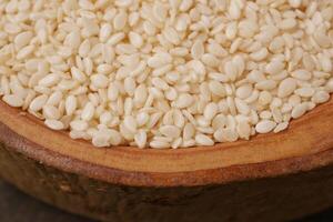 A closeup image showing raw white sesame seeds neatly displayed in a rustic wooden bowl photo