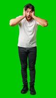 A man with a surprised expression holds his face while against a vibrant green background photo