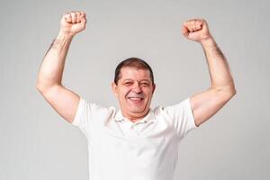 Happy older man showing off his strong biceps while standing against a light gray background photo