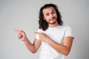 Young man in a white t-shirt and jeans pointing confidently while smiling in a studio setting photo