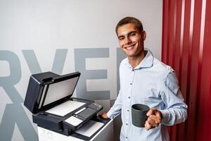 Positive young man using printer in the modern office photo