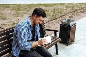 A person writes in a notebook while sitting on a park bench photo