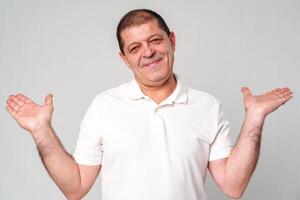 Smiling man in a white shirt gestures with open palms against a light gray background photo