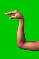 A hand making a gesture with a green background during daylight photo