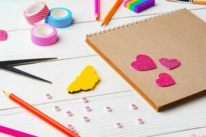 Arts and crafts workspace with colorful supplies, stickers, and a blank notepad on white wooden table photo