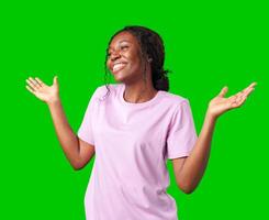 A young woman in casual attire smiles playfully with hands raised in a questioning gesture against a bright green background photo