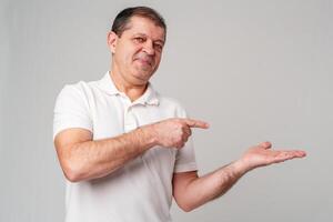 Man dressed in a white polo shirt and jeans happily pointing to the side against a plain background photo