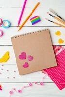Arts and crafts workspace with colorful supplies, stickers, and a blank notepad on white wooden table photo